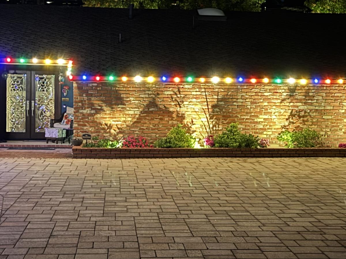 Multicolor roofline lights above a brick wall and a paver driveway