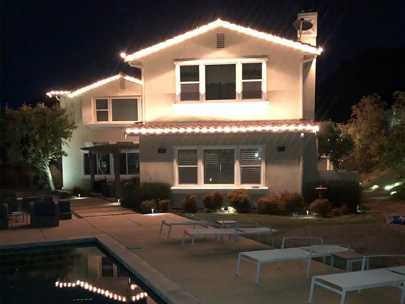 Simi Valley home with warm white roofline lights reflected in a pool