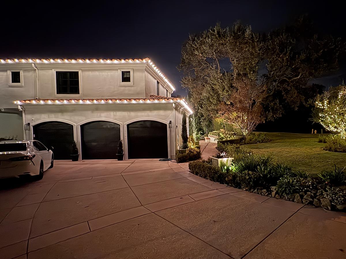 Spanish-style home in the Conejo Valley with warm white roofline lights and a lit olive tree