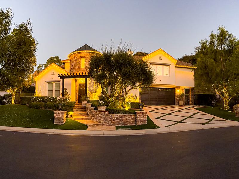 Home at dusk with warm white roofline lights and wrapped tree trunks