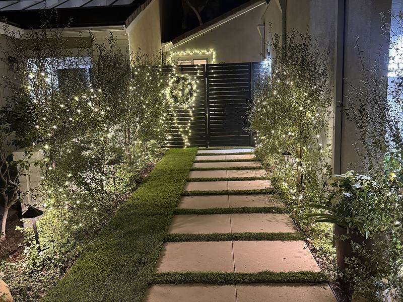 Garden path in Westlake Village with lit shrubs and a lighted wreath on the gate