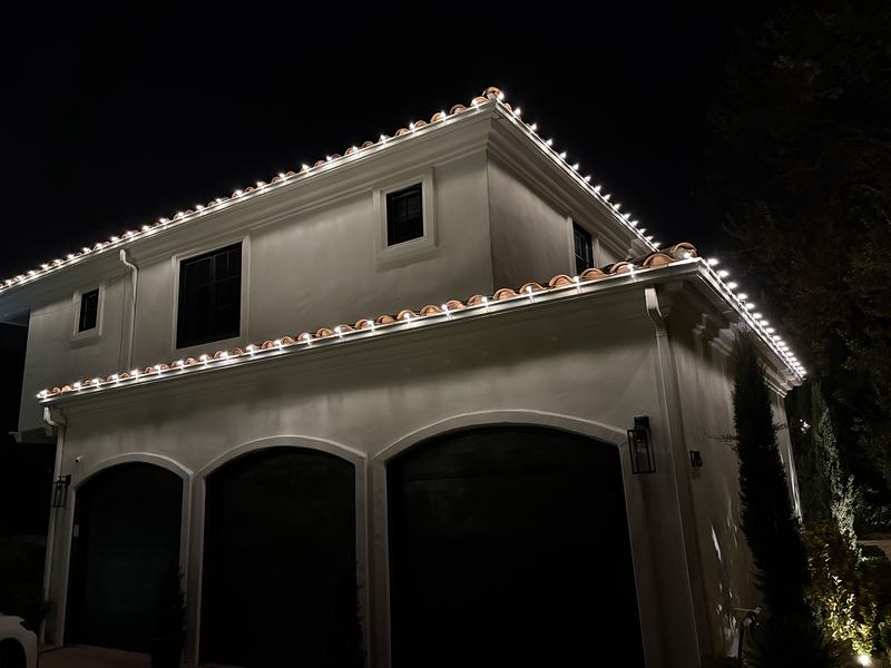 White lights in straight lines along a clay tile roof above arched garage doors